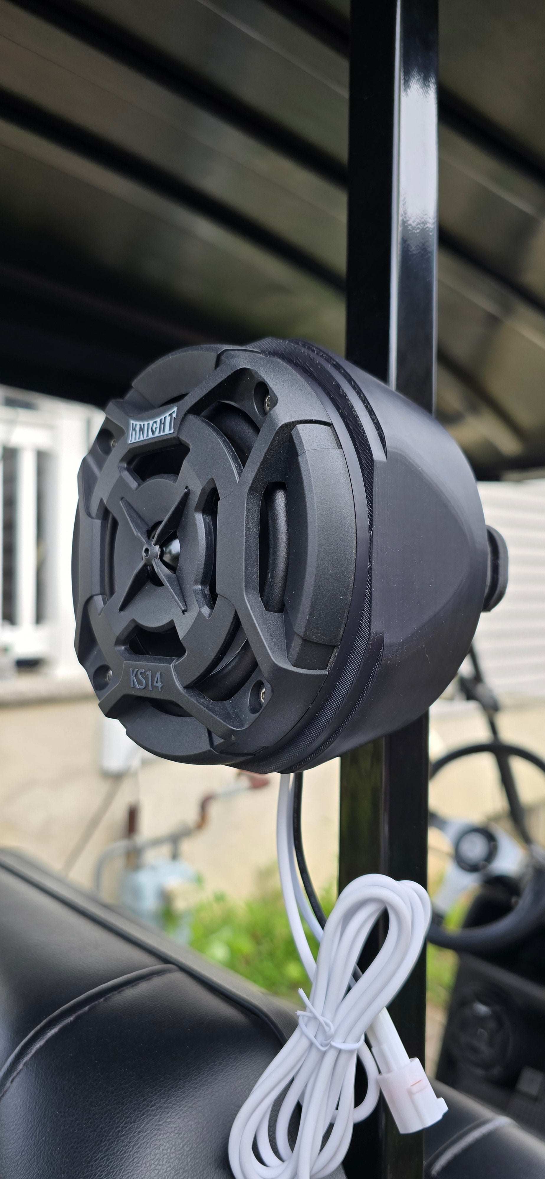 Black outdoor speaker attached to a metal railing with a blurred background