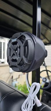 Black outdoor speaker attached to a metal railing with a blurred background